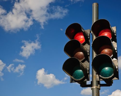 A couple of traffic lights installations with the red ones turned on and the green and yellow off captured against a blue sky with several white clouds scattered over.